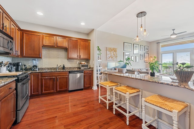 kitchen with dark wood-style flooring, appliances with stainless steel finishes, stone countertops, tasteful backsplash, and a kitchen bar