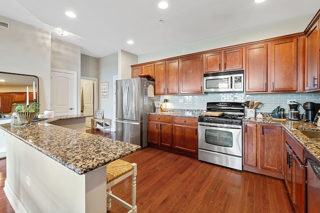 kitchen featuring decorative backsplash, light stone countertops, dark wood-style floors, brown cabinets, and stainless steel appliances