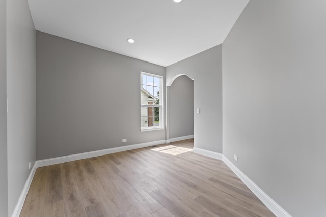 spare room with arched walkways, baseboards, and light wood-style flooring