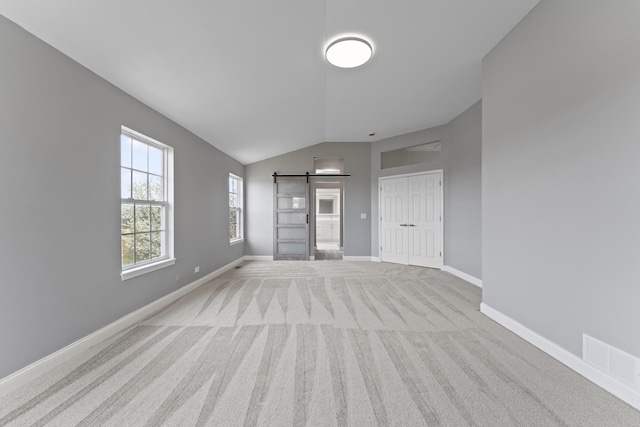 spare room with carpet floors, visible vents, lofted ceiling, baseboards, and a barn door
