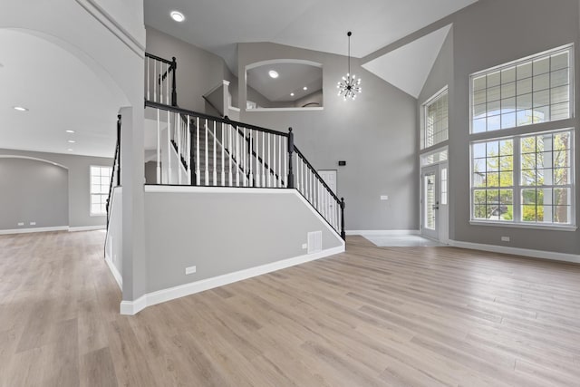 foyer entrance with arched walkways, wood finished floors, baseboards, high vaulted ceiling, and stairs
