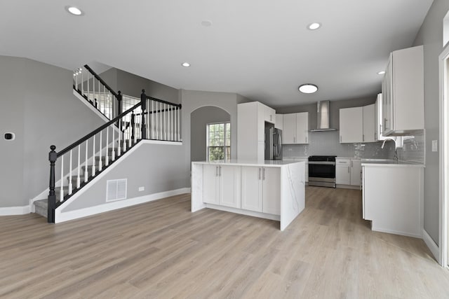 kitchen featuring visible vents, appliances with stainless steel finishes, arched walkways, light countertops, and wall chimney exhaust hood