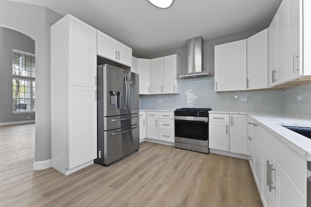 kitchen with white cabinetry, baseboards, light wood-style floors, stainless steel appliances, and wall chimney exhaust hood
