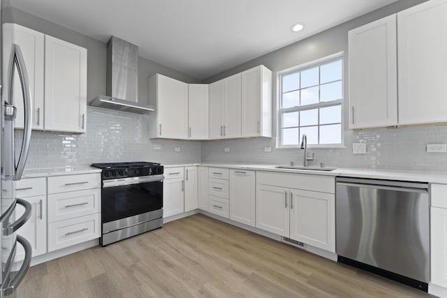 kitchen with wall chimney range hood, light countertops, a sink, light wood-style flooring, and stainless steel appliances