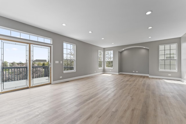 unfurnished living room featuring recessed lighting, arched walkways, light wood-style flooring, and baseboards