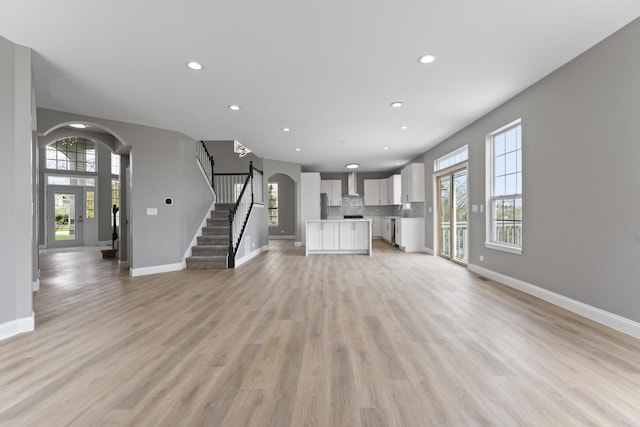 unfurnished living room with baseboards, arched walkways, recessed lighting, and stairway