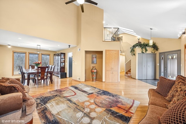 living area with light wood-style flooring, stairs, a ceiling fan, and high vaulted ceiling