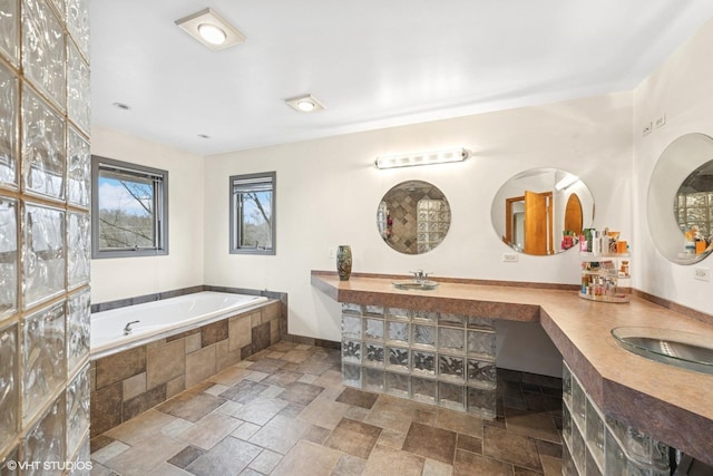 bathroom with stone tile flooring, a sink, a bath, and double vanity