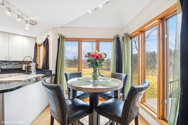 dining space with rail lighting, light wood-style flooring, and lofted ceiling