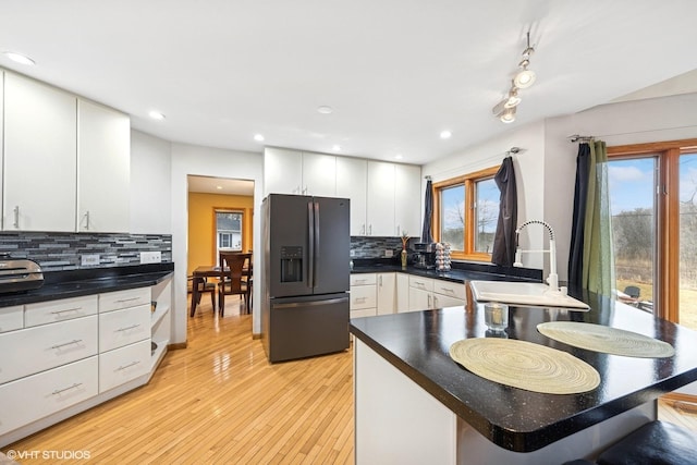 kitchen with dark countertops, light wood-style floors, fridge with ice dispenser, tasteful backsplash, and a sink