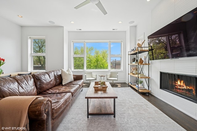 living area with wood finished floors, a warm lit fireplace, a ceiling fan, and recessed lighting
