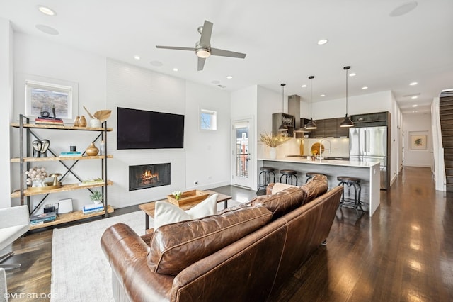living room featuring dark wood-style floors, ceiling fan, a large fireplace, baseboards, and recessed lighting