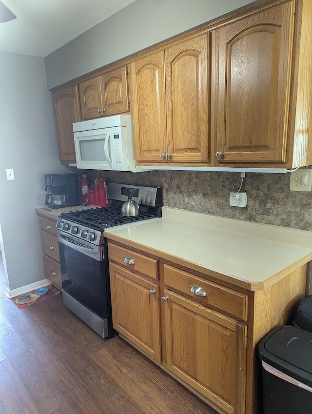 kitchen with light countertops, brown cabinetry, stainless steel range with gas cooktop, white microwave, and dark wood-style floors