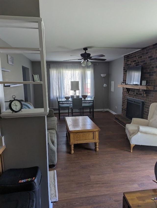 living area featuring a ceiling fan, baseboards, dark wood finished floors, and a fireplace