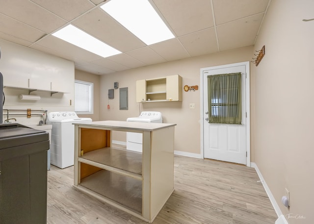 clothes washing area with cabinet space, baseboards, light wood-type flooring, washing machine and dryer, and electric panel