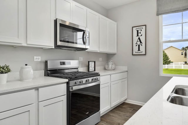 kitchen with light stone countertops, dark wood-type flooring, white cabinetry, a sink, and appliances with stainless steel finishes
