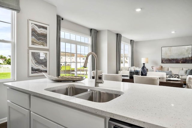 kitchen with light stone counters, a sink, white cabinetry, open floor plan, and recessed lighting