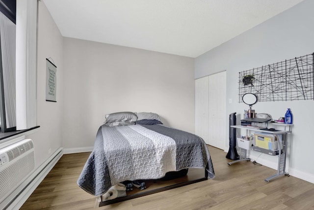 bedroom with baseboards, baseboard heating, a closet, and wood finished floors