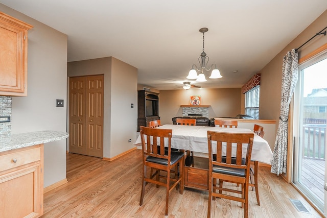 1678 Eagles Lndg N, Manteno, IL 60950 - dining space featuring a stone fireplace, light wood-style flooring, a chandelier, and ceiling fan