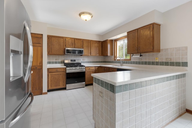 kitchen with brown cabinetry, a peninsula, light countertops, a sink, and appliances with stainless steel finishes