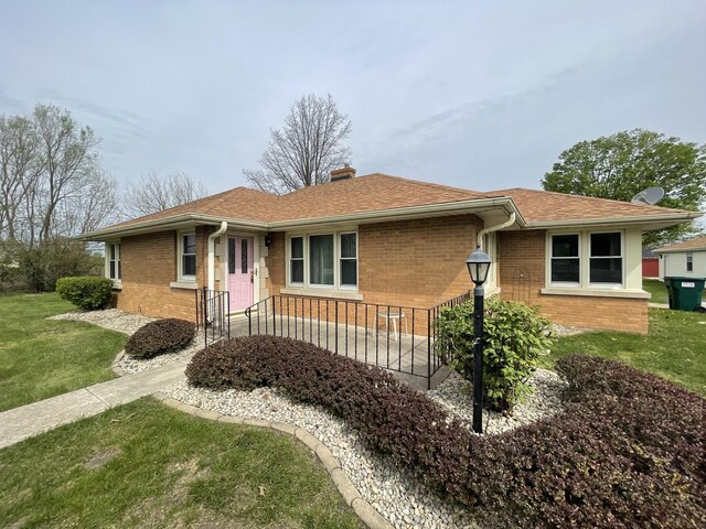 ranch-style home with roof with shingles, a front lawn, a chimney, and brick siding