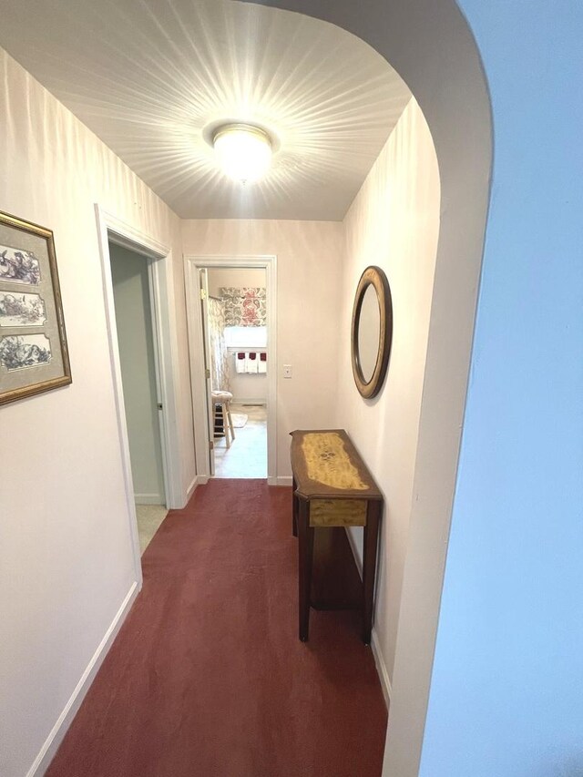 hallway with carpet flooring, baseboards, and arched walkways