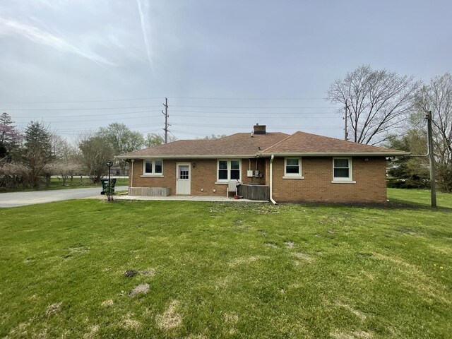 back of house with a chimney, brick siding, and a lawn