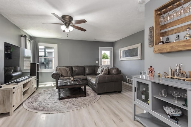 living room featuring ceiling fan, visible vents, baseboards, and light wood finished floors