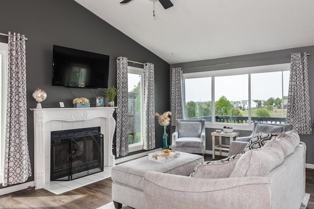 living room with a tiled fireplace, a ceiling fan, baseboards, wood finished floors, and vaulted ceiling