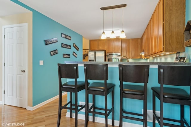 5515 Mcdonough Rd Unit 5515, Hoffman Estates, IL 60192 - kitchen featuring stainless steel appliances, light wood-style flooring, brown cabinets, decorative light fixtures, and a peninsula