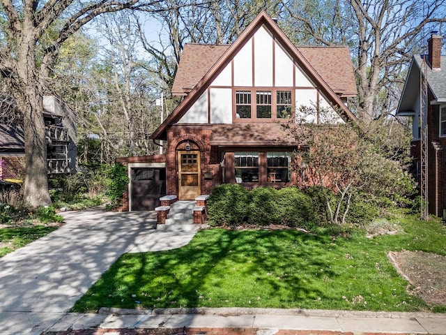 tudor house featuring roof with shingles, brick siding, stucco siding, a front yard, and driveway
