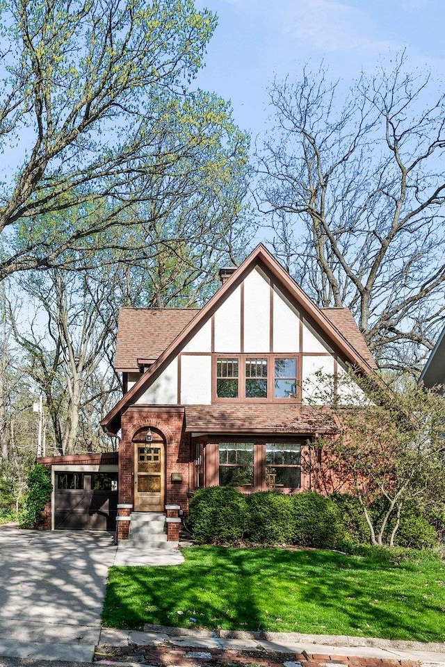 tudor-style house featuring a front yard, a carport, concrete driveway, a shingled roof, and stucco siding