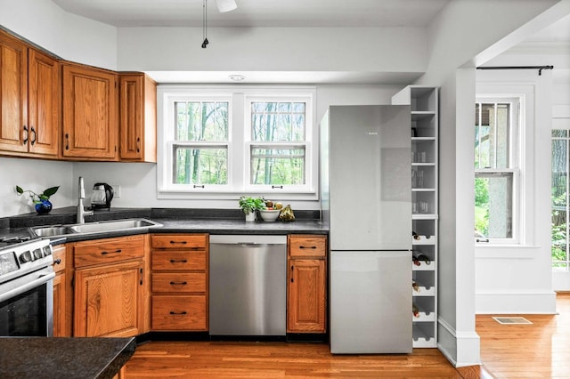 kitchen with a sink, appliances with stainless steel finishes, brown cabinets, and wood finished floors