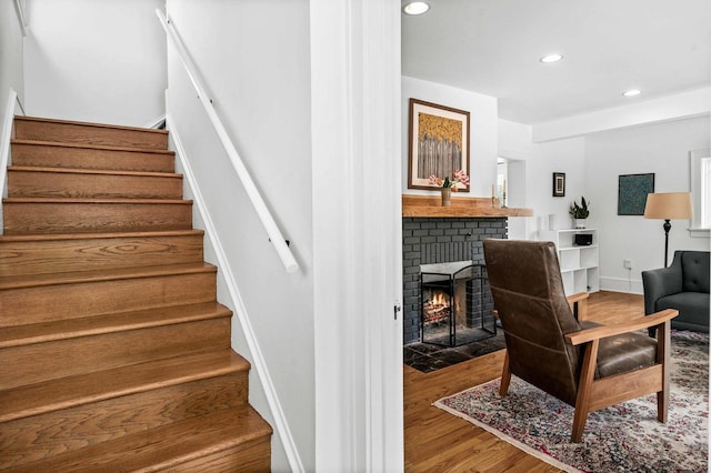 stairway featuring recessed lighting, a brick fireplace, and wood finished floors
