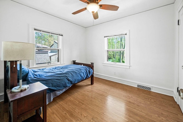 bedroom with baseboards, a ceiling fan, wood finished floors, and visible vents