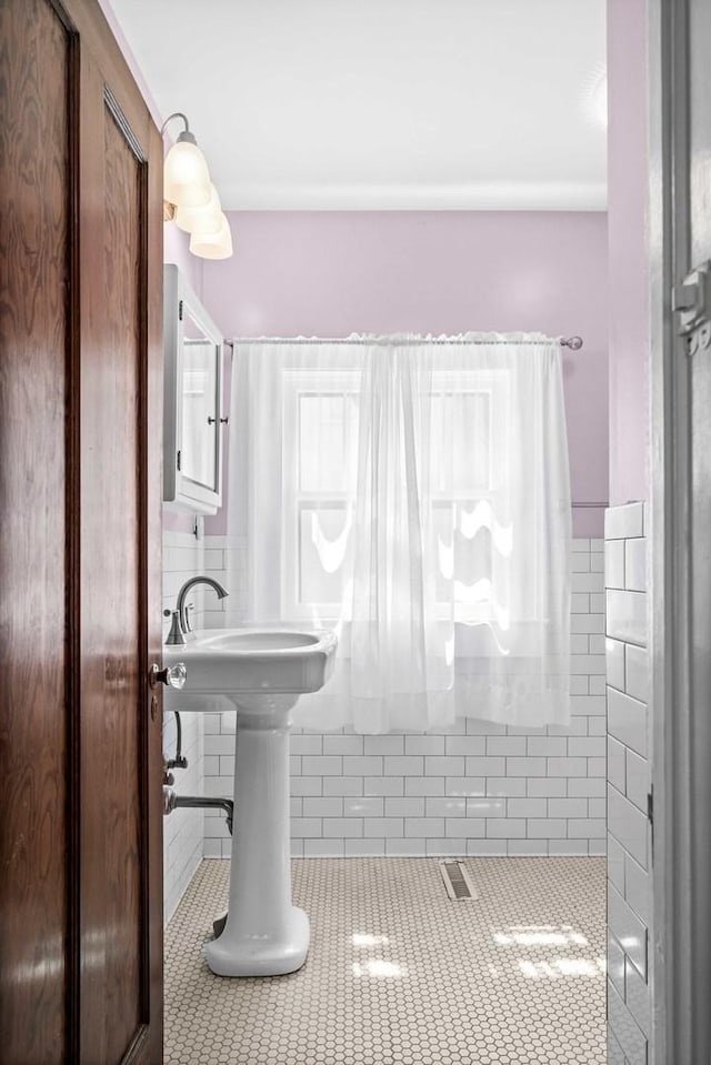 bathroom featuring tile patterned floors, tile walls, a sink, and a wainscoted wall