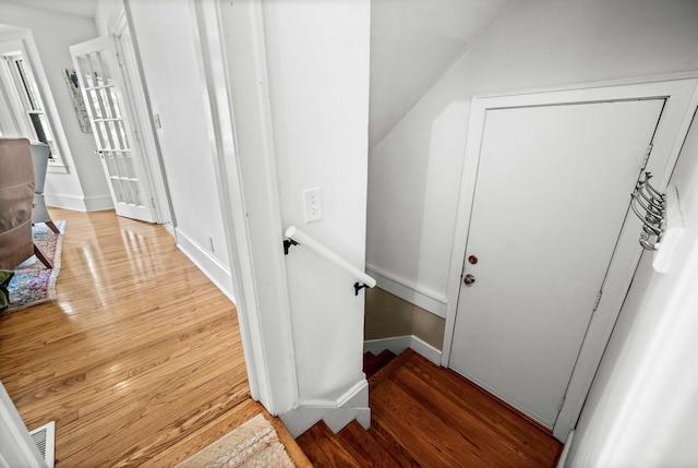 hallway with visible vents, light wood-style floors, baseboards, vaulted ceiling, and an upstairs landing