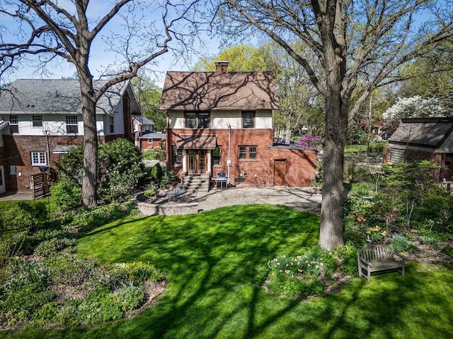 back of property with brick siding, french doors, a chimney, a lawn, and a patio