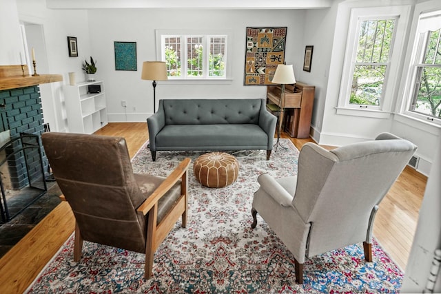 living area with baseboards, a brick fireplace, and wood finished floors