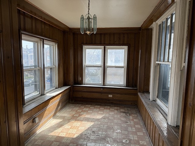 interior space with ornamental molding, wooden walls, and a chandelier