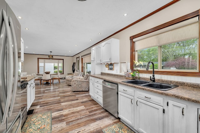 kitchen featuring crown molding, a sink, white cabinets, stainless steel appliances, and light wood-style flooring