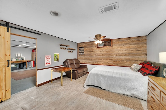 bedroom with wood walls, visible vents, a barn door, and an accent wall