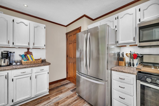 kitchen featuring white cabinets, appliances with stainless steel finishes, a textured ceiling, wood finished floors, and ornamental molding