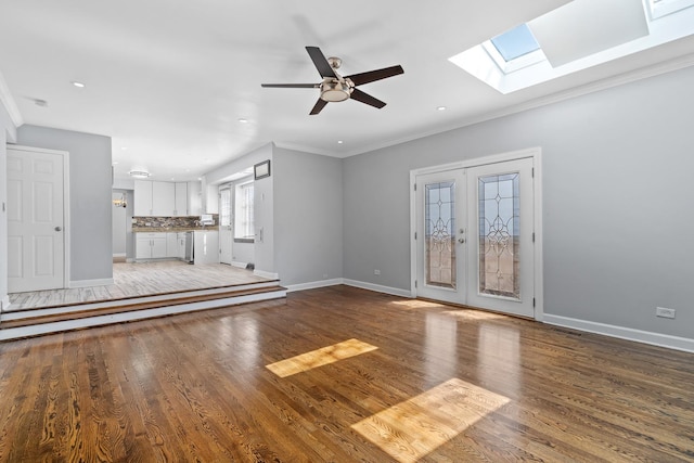 unfurnished living room with crown molding, wood finished floors, baseboards, a ceiling fan, and a skylight