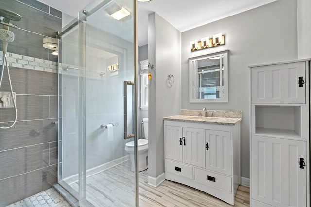 bathroom with vanity, wood finished floors, toilet, baseboards, and a shower stall