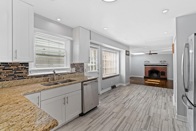 kitchen with decorative backsplash, a ceiling fan, a fireplace, a sink, and stainless steel appliances