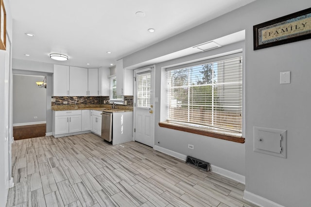 kitchen with white cabinets, a sink, dishwasher, baseboards, and decorative backsplash