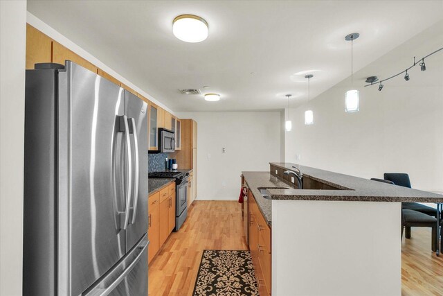 kitchen featuring stainless steel appliances, dark countertops, a sink, and light wood-style flooring