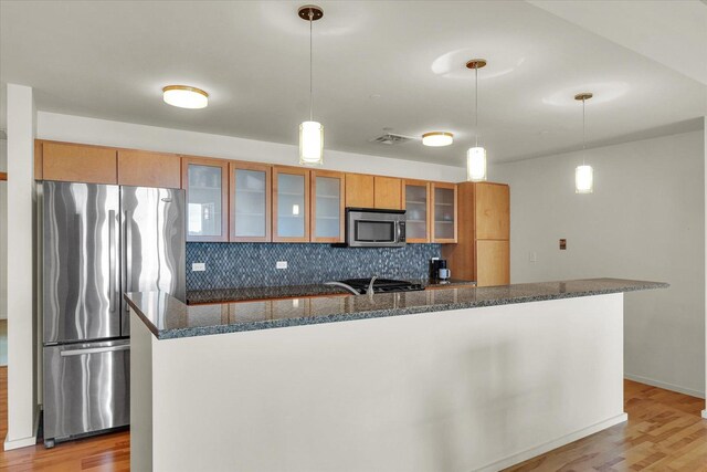 kitchen with appliances with stainless steel finishes, light wood-style flooring, backsplash, and brown cabinetry