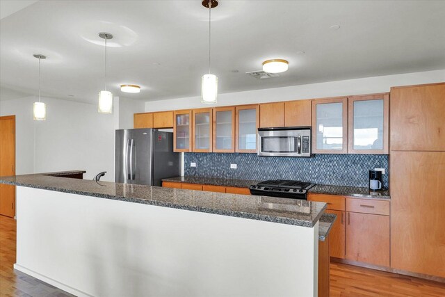 kitchen with appliances with stainless steel finishes, decorative backsplash, light wood-style flooring, and glass insert cabinets